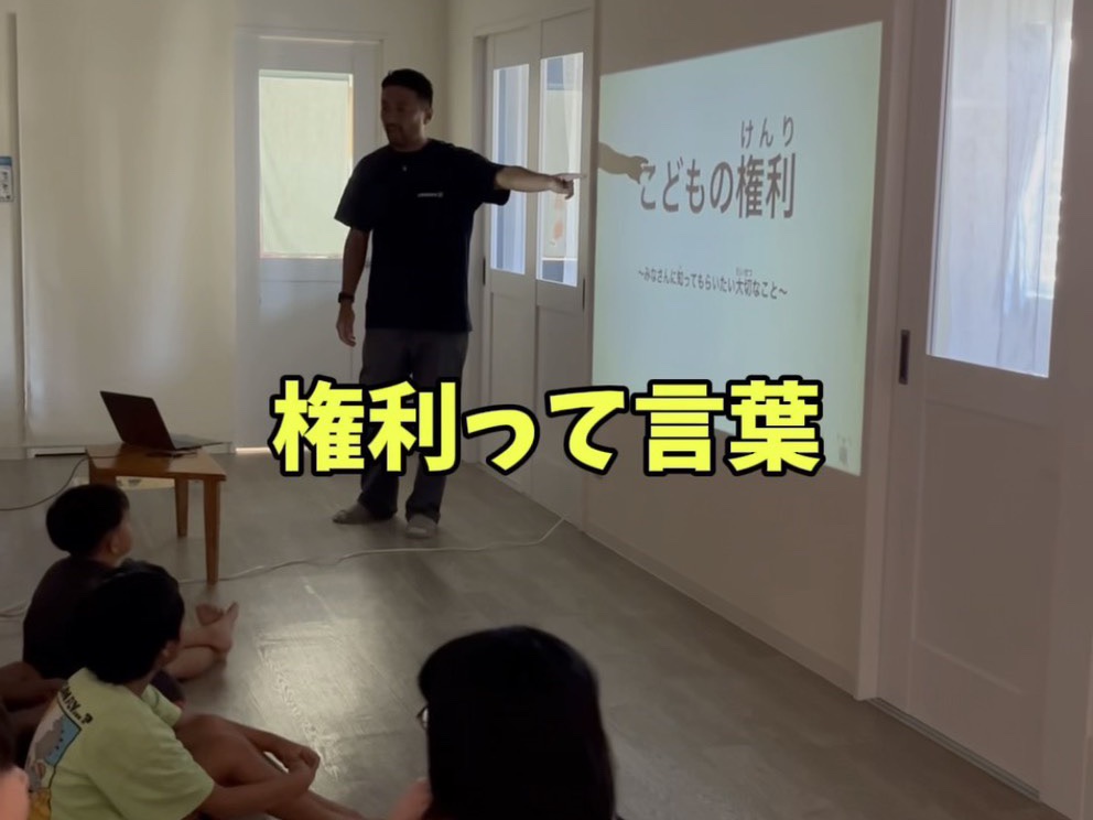 「こどもの権利」のスライドを前に子どもたちへ話す代表（2026年7月28日・うるま市）