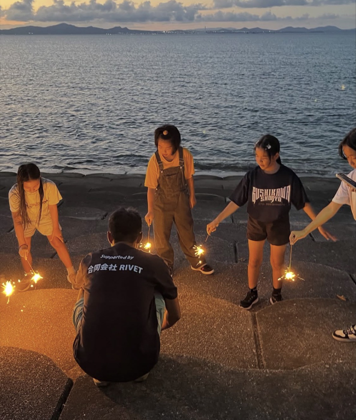 夕暮れの海辺で花火をする子どもたち（お泊まり遠足・2026年7月23〜24日・うるま市宮里）
